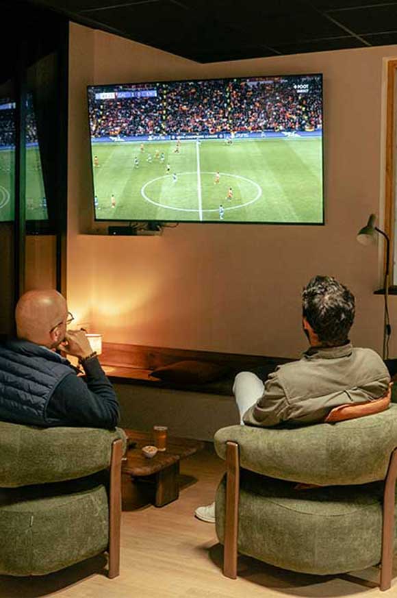 Personnes assises dans des fauteuils regardant un match à la télévision dans le club house de Pure Padel La roche sur Yon