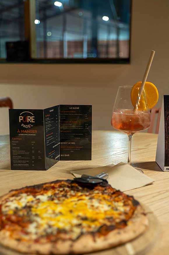 Pizza et cocktail servis dans le club house avec vue sur les pistes de padel. Pure Padel La Roche sur Yon